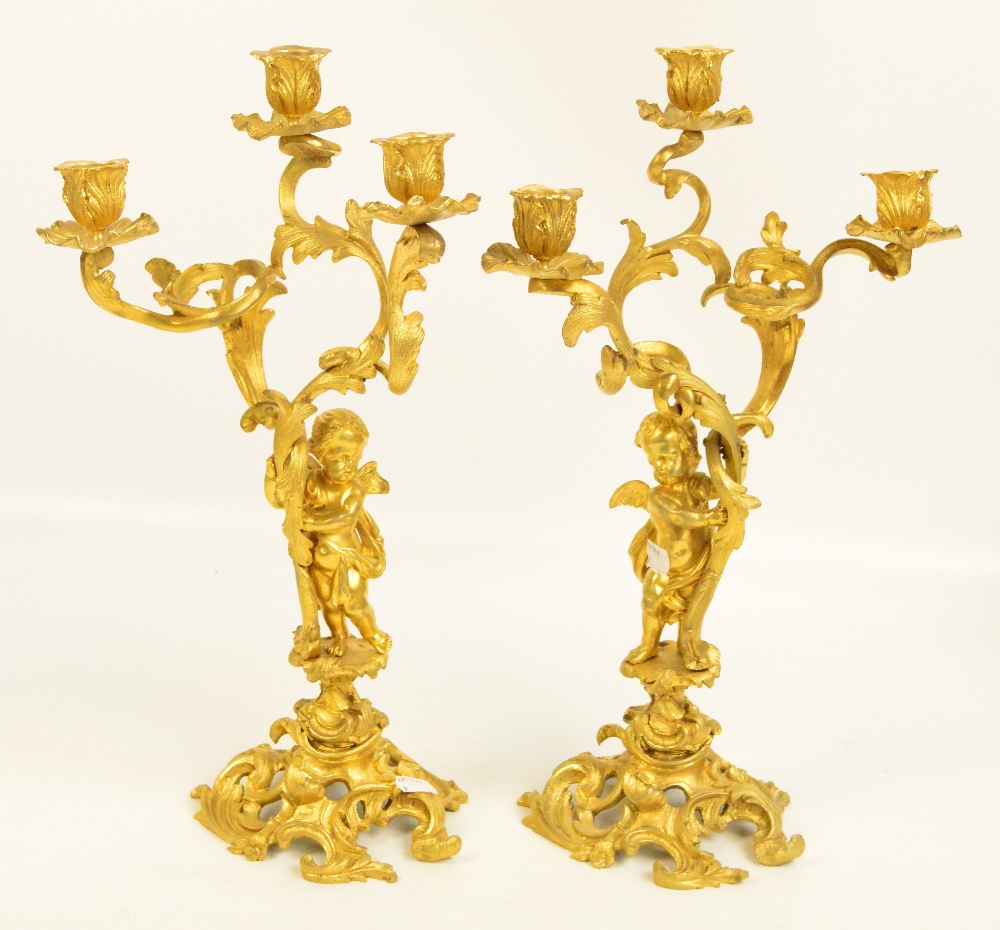A pair of gilt metal rococo style three branch candelabra decorated with cherubs amongst scrolling