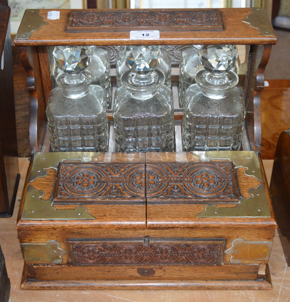 An Edwardian oak and metal banded tantalus box, the raised back with three moulded decanters above