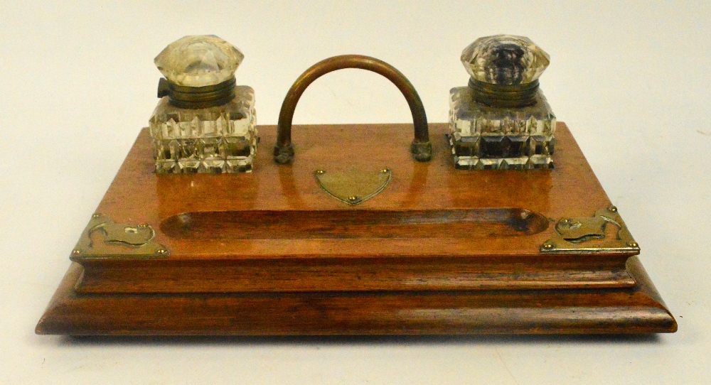 A late Victorian oak brass mounted inkstand with twin hobnail cut glass wells above a vacant shield,