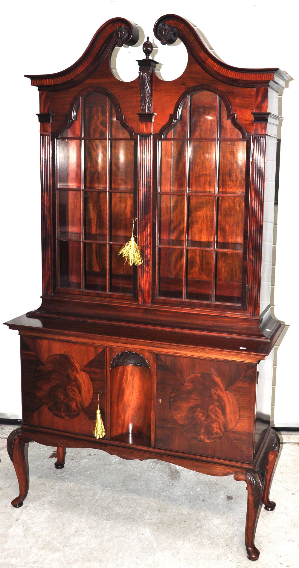 A reproduction mahogany bookcase, the carved broken swan neck pediment above twin arched doors