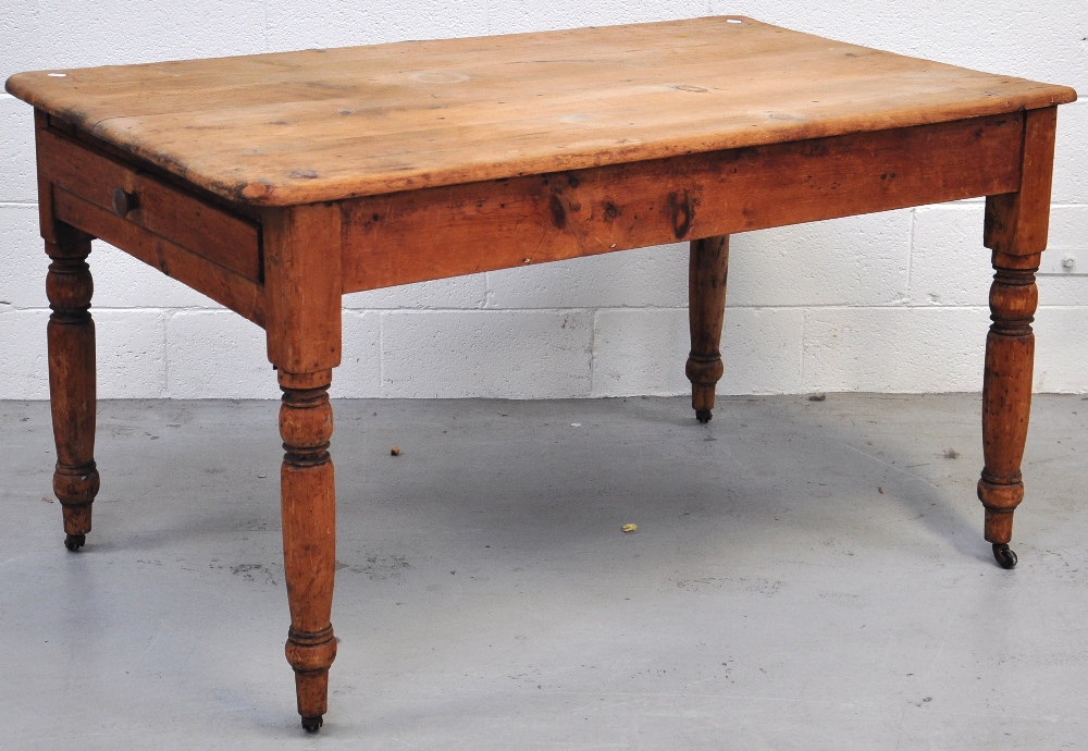 A rustic pine kitchen table with single drawer on ring turned supports and original castors,