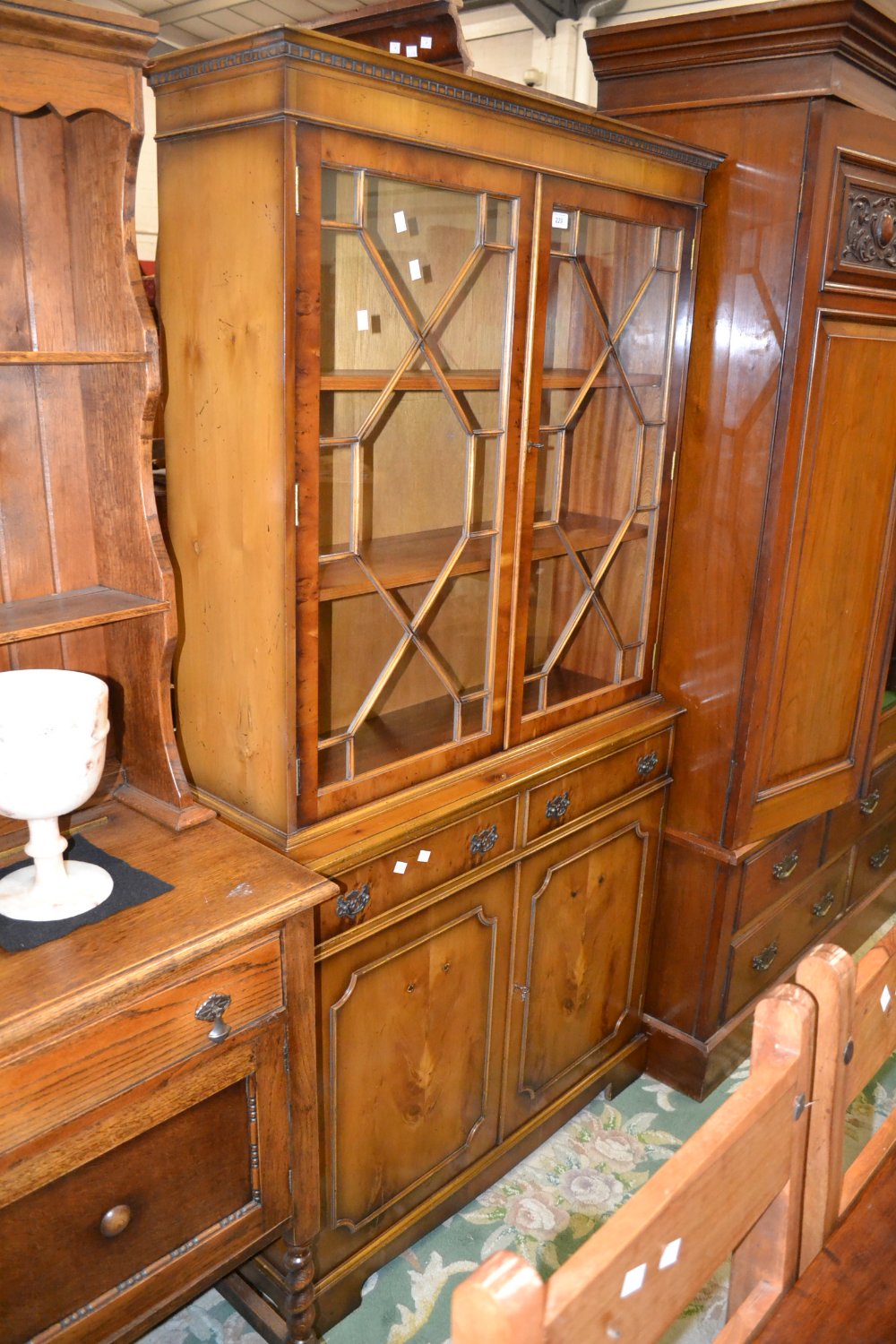 A reproduction yew veneered bookcase cabinet, dentil cornice, astragal glazed doors enclosing