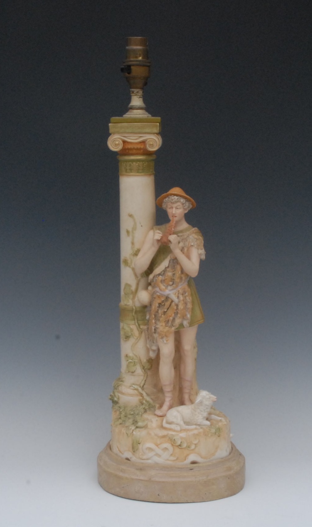 A Royal Dux figural table lamp, modelled as a shepherd boy beside an Ionic column, he stands,