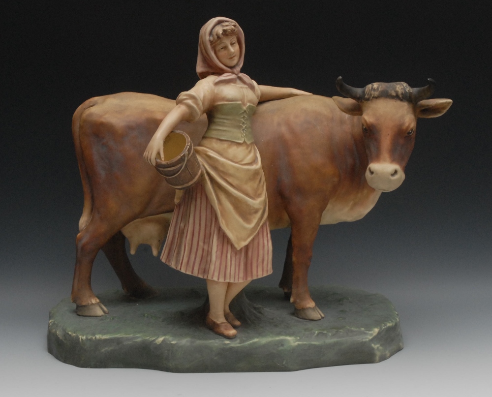 A Royal Dux model of a milkmaid and cow, she stands holding a coppered pail, her arm on a horned