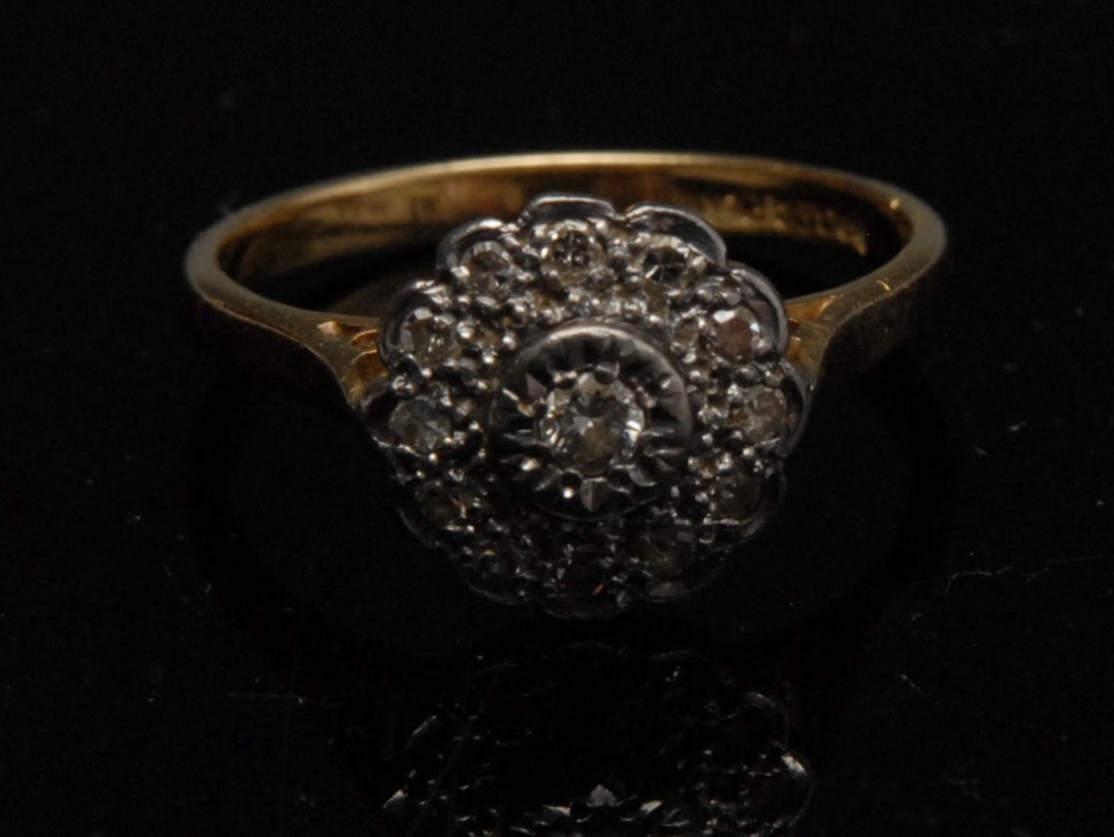 A diamond flowerhead ring, central raised collet set diamond, set within a band of twelve further