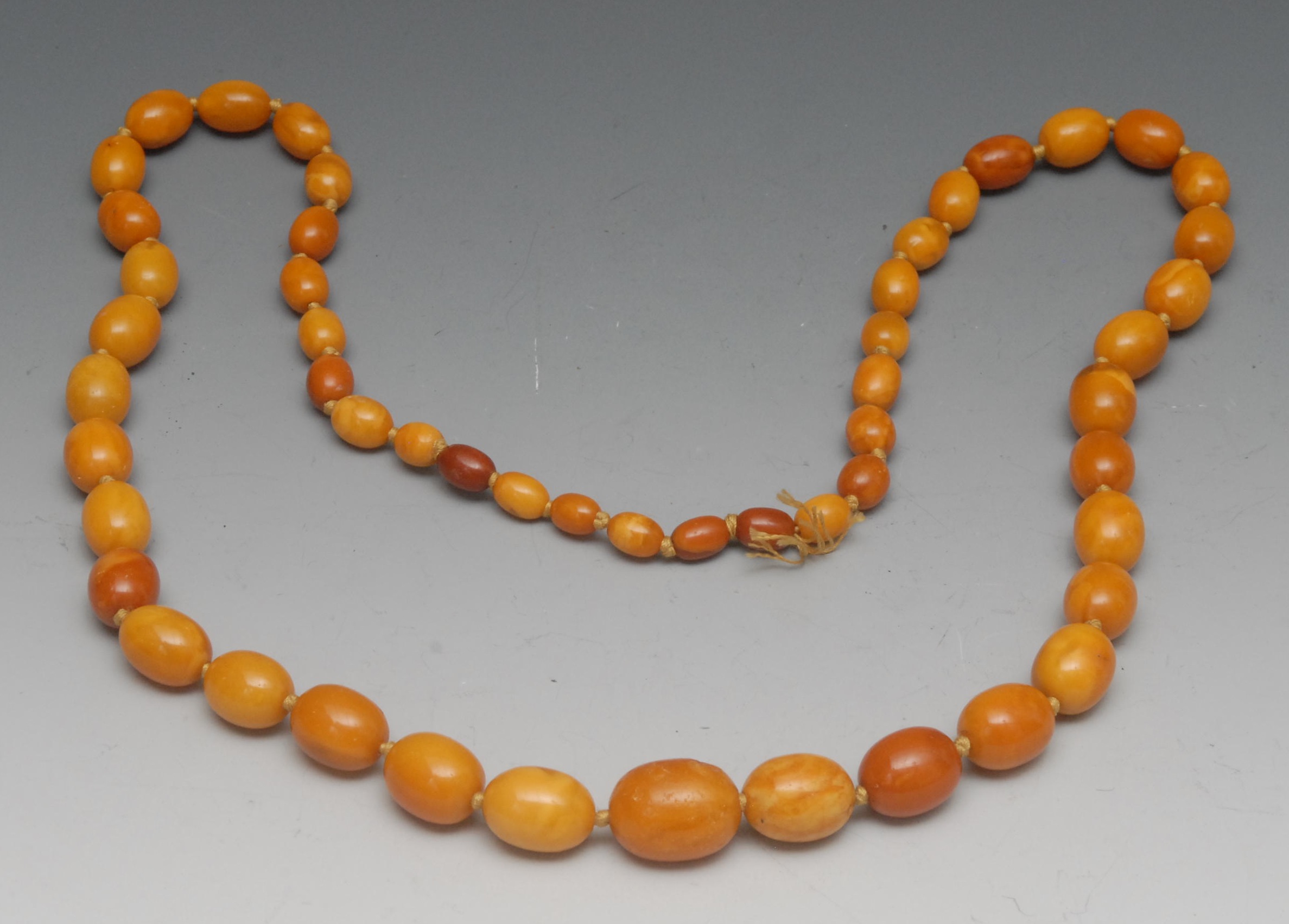 A graduated amber bead necklace, fifty-three graduated beads, of mottled yellow and butterscotch