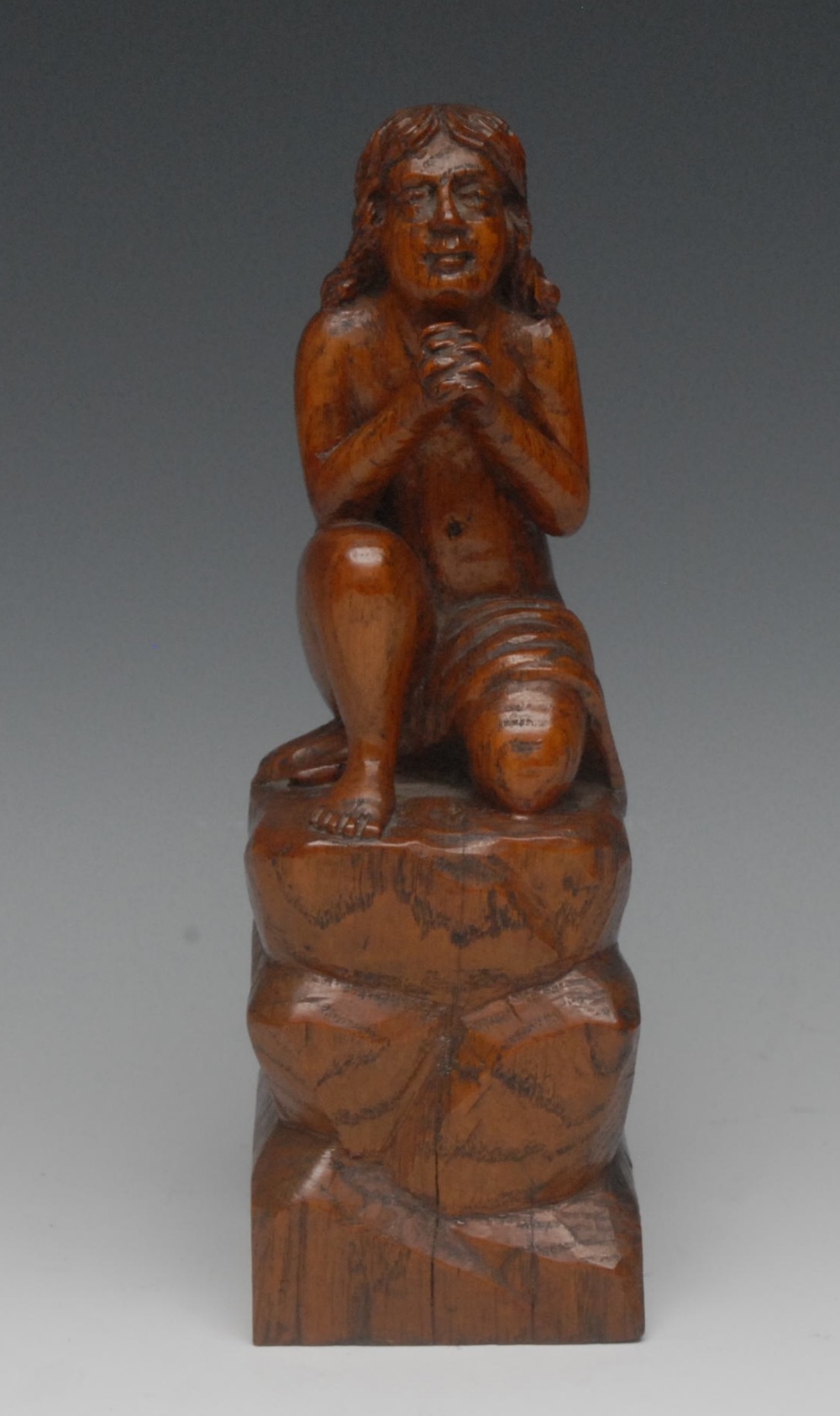 A North European oak carving, of a scantily clad figure, kneeling, atop a rock, 24cm high