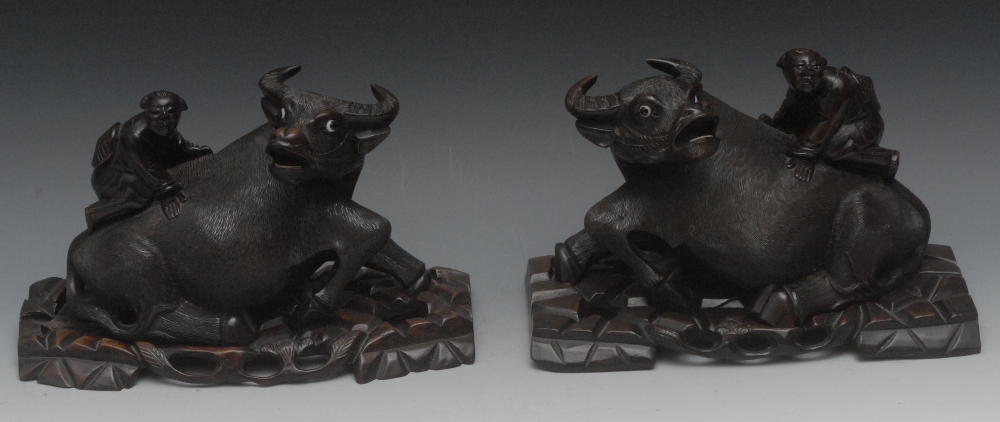 A pair of Chinese hardwood carvings, of boys riding buffaloes,   pierced padouk wood stands, 26cm