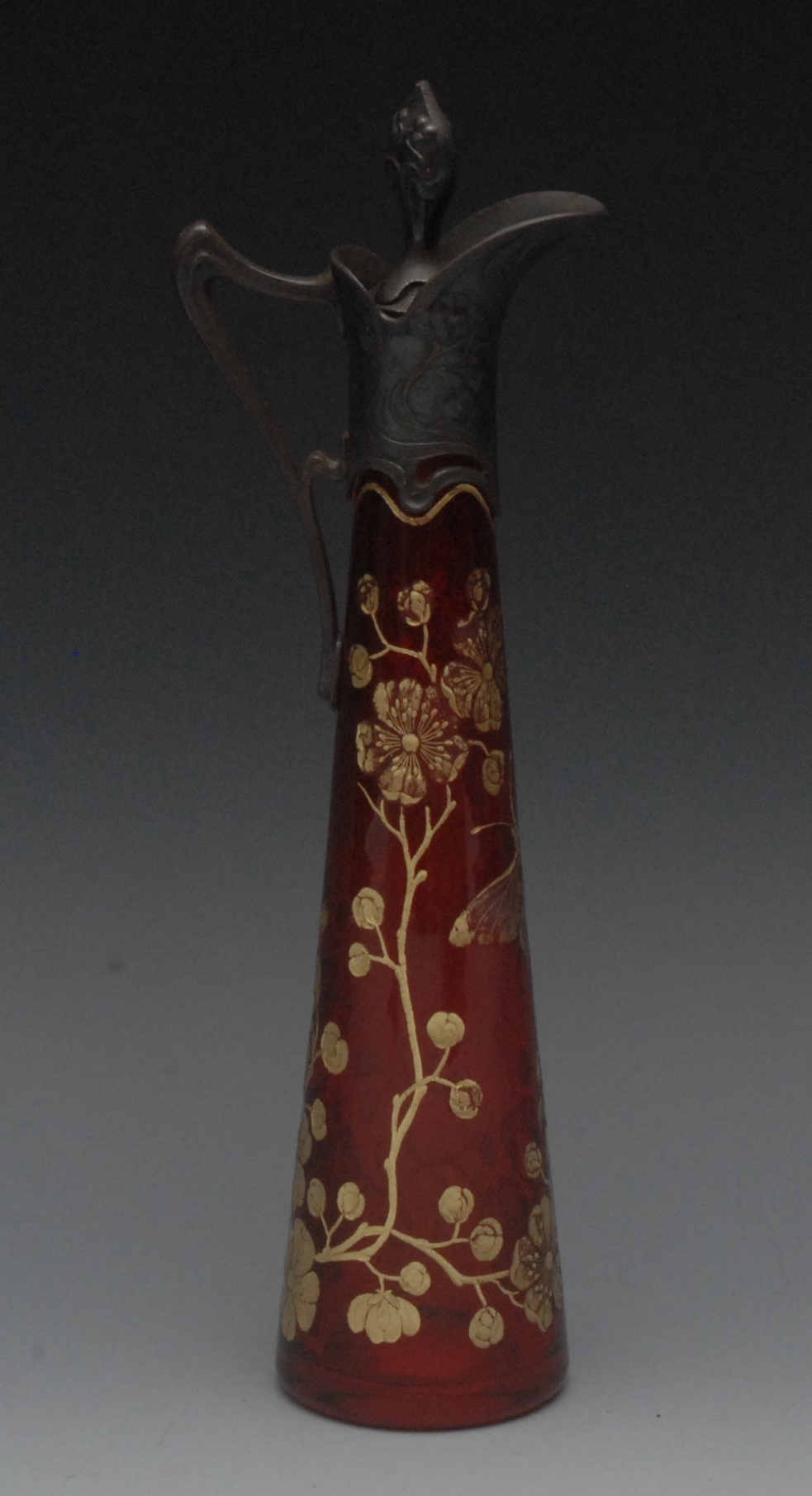A slender cylindrical cranberry ewer, engraved with butterfly and foliage, pewter spout, sinuous