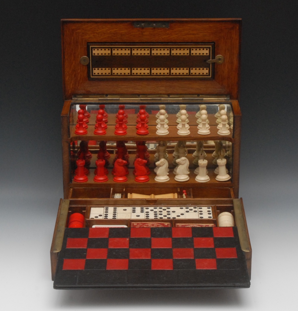 A Victorian oak games compendium, hinged cover and fall front enclosing mirrored tiers and spring