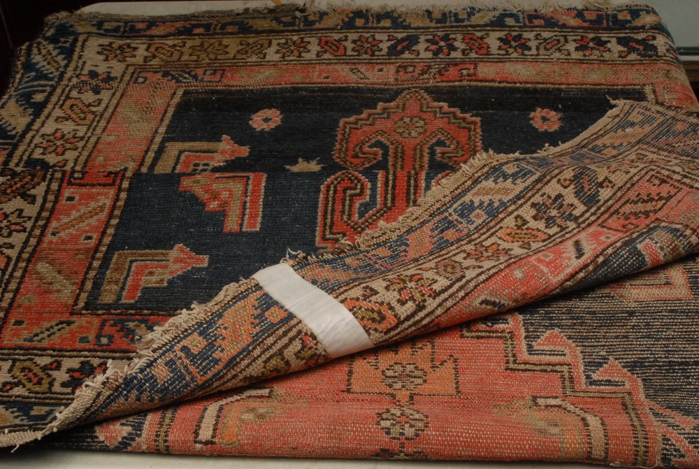 A Middle Eastern rectangular woollen rug, the field with a large hooked medallion, worked in tones