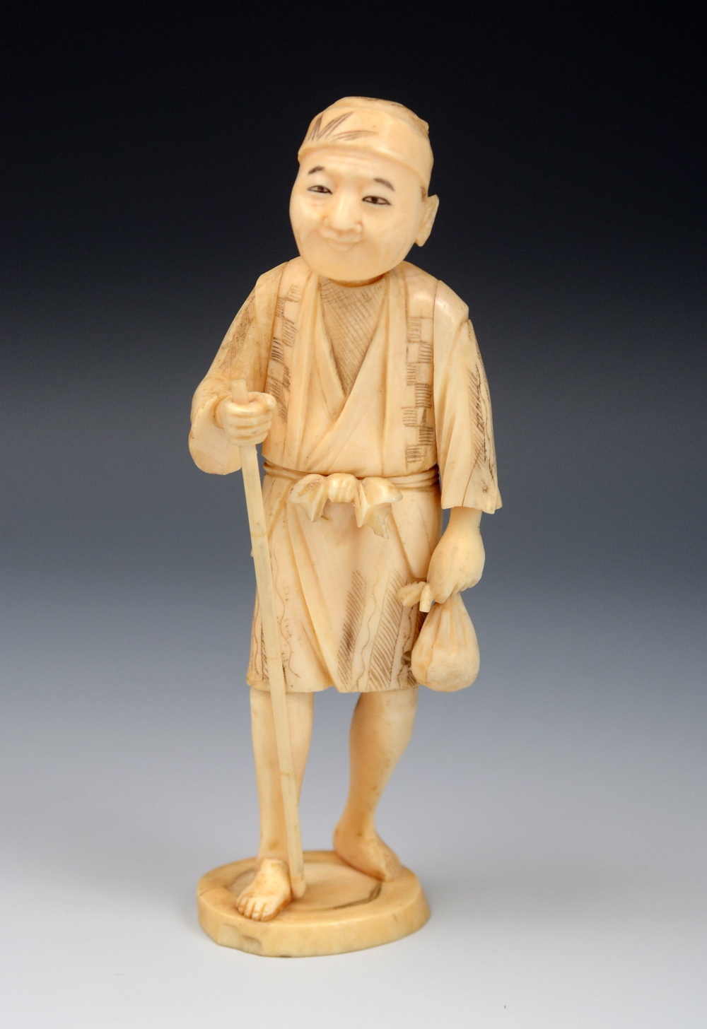 A Japanese ivory okimono, of a labourer en-route to the field, gripping a staff in one hand, his