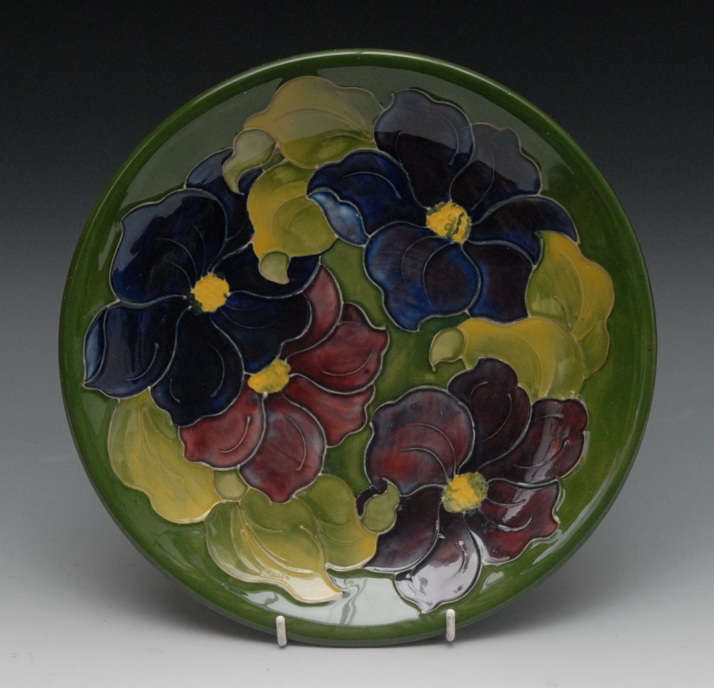 A Moorcroft Hibiscus pattern plate, tube lined with large flowers and foliage, on a green ground,