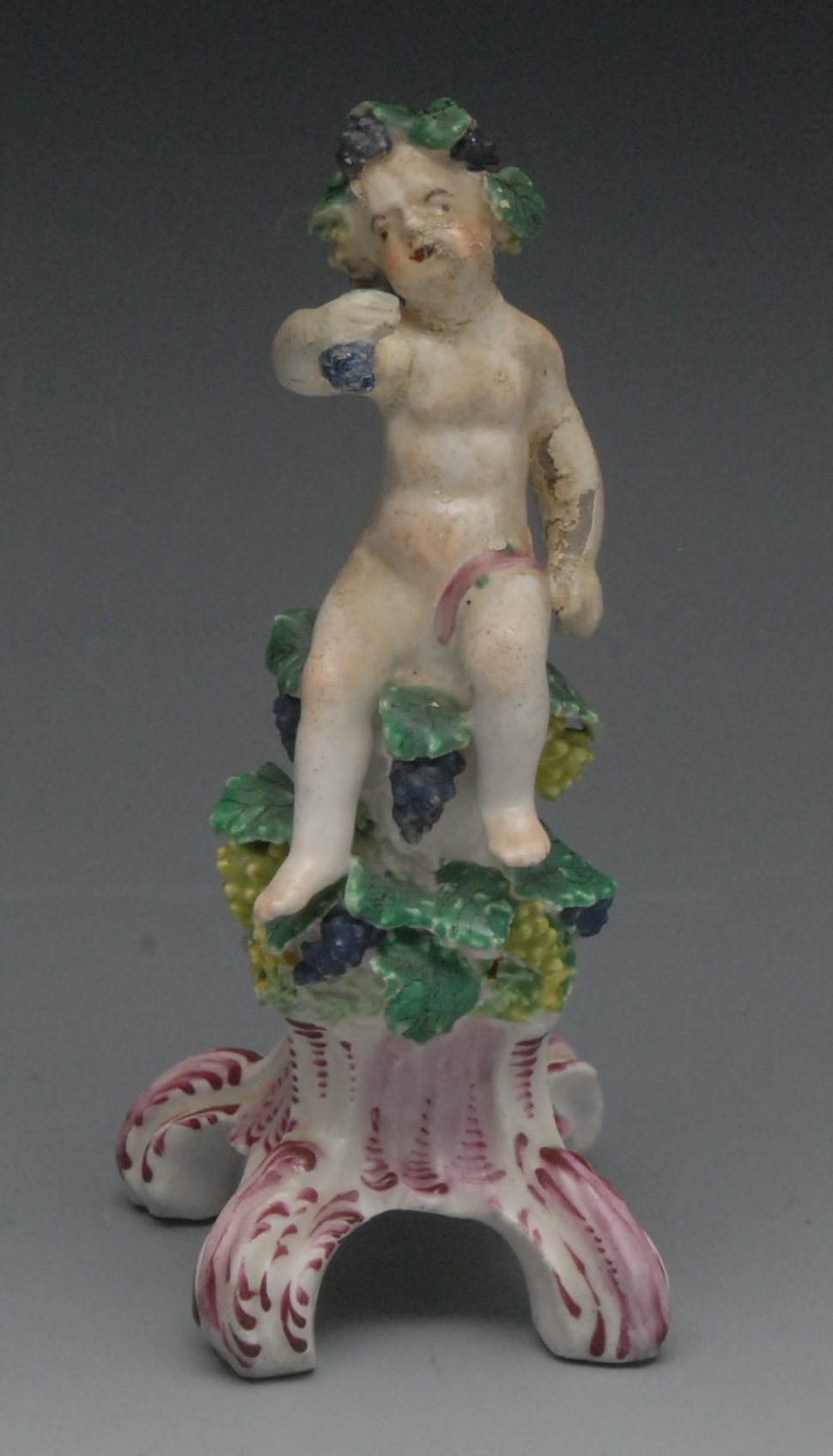 A Bow figure, Allegorical of Autumn, as a cherub with vine chaplet, seated on a vine mound, scroll