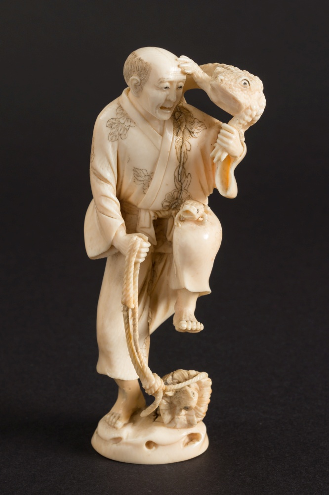 A Japanese carved ivory figure of Gama Sennin: an overturned basket at his feet and toads on his