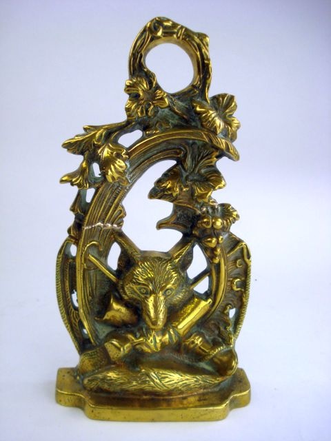 A brass fox hunt theme door stop:, in the form of a fox mask, riding crop and boots within a floral