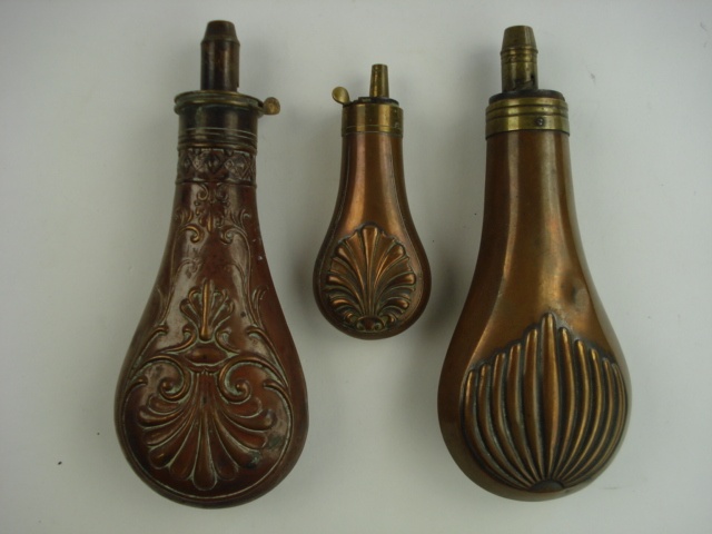 A various copper and brass three powder flasks:, with embossed decoration.