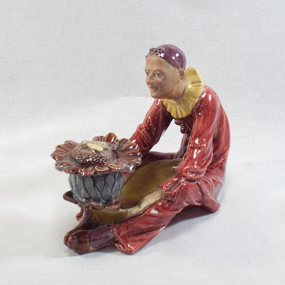 Austrian figure of a seated pierrot holding a flower shaped ink well surmounted by a bee, circa