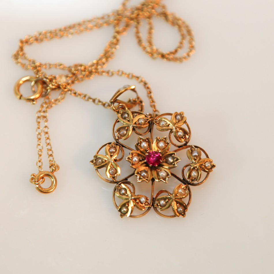 Edwardian 9ct yellow gold flower design pendant set with seed pearls and red stone on a long 9ct