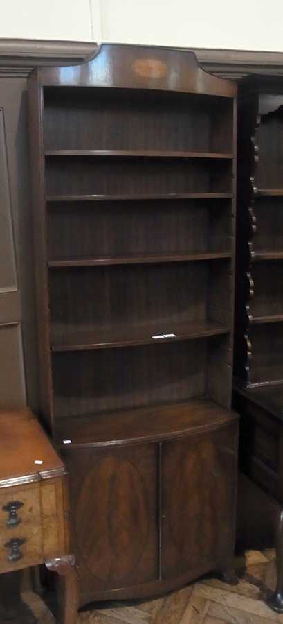 A Sheraton style mahogany bow-front open bookcase, adjustable shelves, with cupboard below, raised