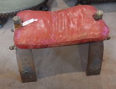 A Middle Eastern camel saddle stool, red leather cushion, on wooden supports