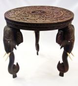 An Indian carved hardwood circular occasional table, on elephant mask supports, 46cm diameter