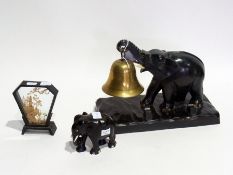 A carved ebony elephant on stand supporting a table bell together with a similar smaller elephant