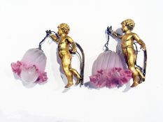 A pair of gold-painted metal cherub wall lights with hanging pink spiral and frill glass shades,