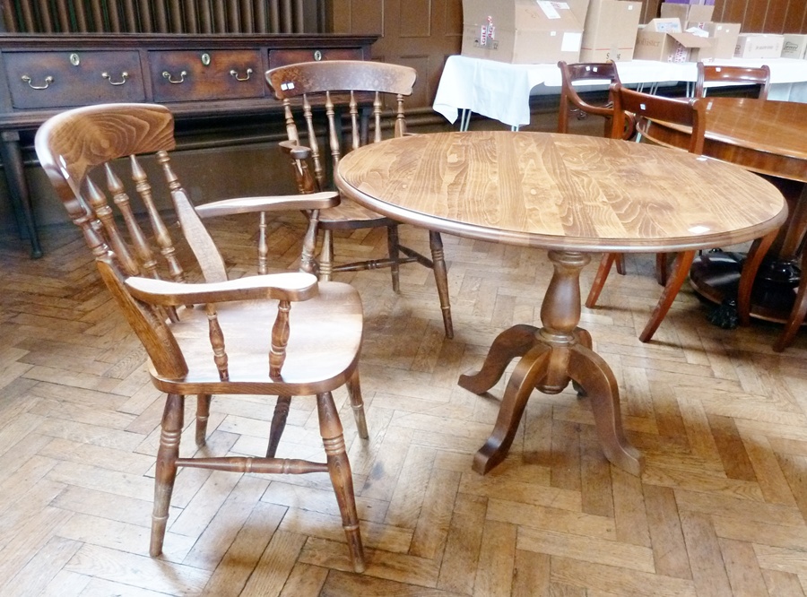 A reproduction stained pine circular-topped dining table on pedestal support with outswept legs,