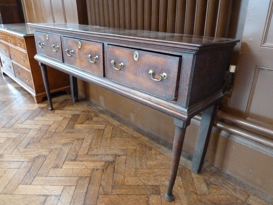 An 18th century oak low dresser with three deep frieze drawers, with brass escutcheons and swan-neck