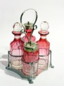 A cut cranberry glass four-bottle condiment set, within a silver plate stand, with paw feet