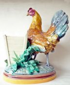 A Minton's majolica model of a chicken standing beside a bin on oval plinth base with vegetation,