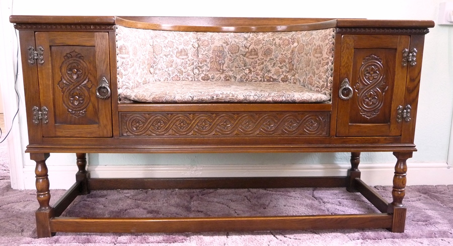 An oak reproduction hall seat with two small cupboards, carved panelled doors, guilloche-style