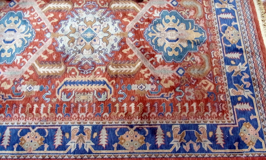 A New Zealand wool carpet, dark red ground, blue border with central medallions, in blue, green