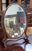 An antique mahogany toilet mirror, oval, on supports, 32cm wide