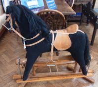 A modern black rocking horse, with harness and saddle, complete with stand, 130cm long