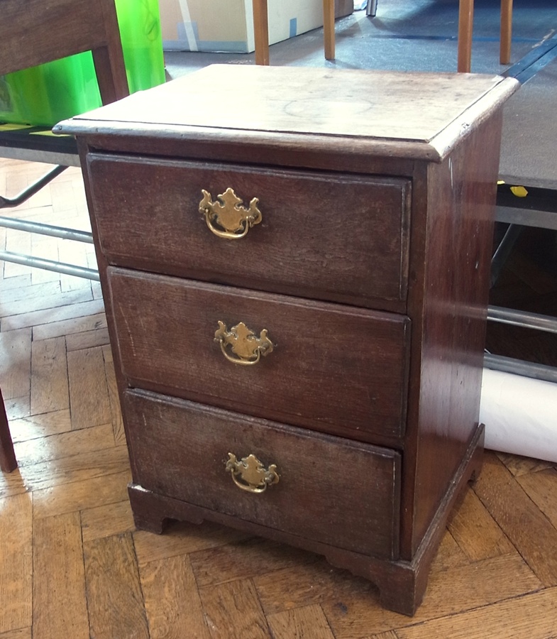 Small oak bedside chest with quadrant mould edge, three drawers with brass drop handles and shaped