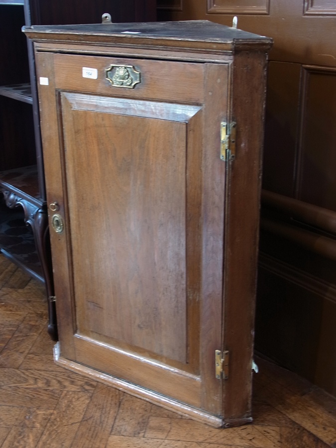 Oak wall hanging corner cabinet with shell embossed brass plaque above the framed panelled door,