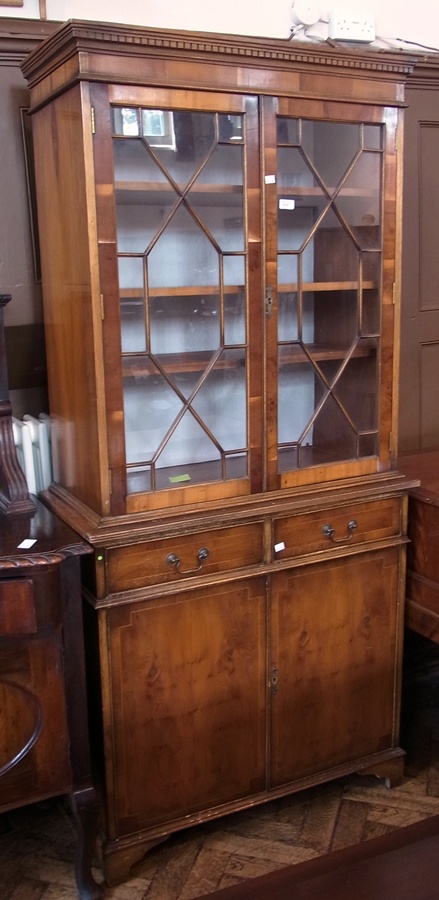 A reproduction Georgian style yew wood veneer bookcase with dentil frieze, the astragal-glazed doors