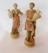 Pair Royal Dux Bohemia male and female figures holding urns on circular plinth base, 30cm high