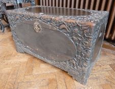 An oriental carved hardwood coffer, hinged lid, heavily decorated, with oval-shaped panel to top and