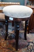 An oak circular swivel piano stool, with cream upholstery, on splayed supports, united by stretcher