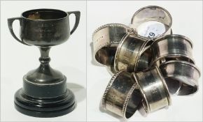 Seven various silver napkin rings and a small silver two-handled cup (6)