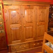 A contemporary pine triple wardrobe with panel door above base drawers W 175 x D 55 x H 197 cm