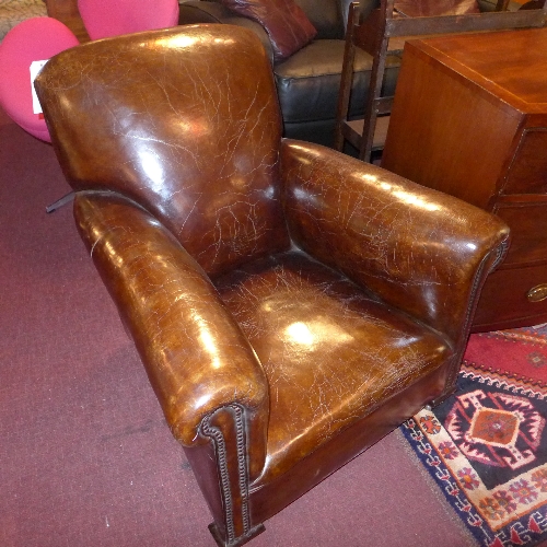 A good pair of early C20th tan leather club chairs with brass studded detail and raised on castors