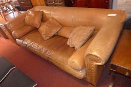 A contemporary designer three seater sofa upholstered in tan leather and with additional cushions