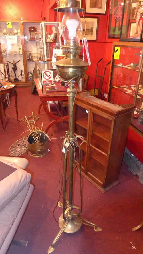An Arts and Crafts brass standard lamp with a glass funnel and reservoir converted to electricity