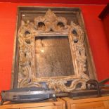 A large looking glass with heavy cast iron scolling leafy frame within square distressed pine frame