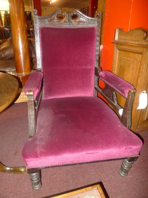A pair of Edwardian carved oak armchairs upholstered in purple velour raised on turned supports