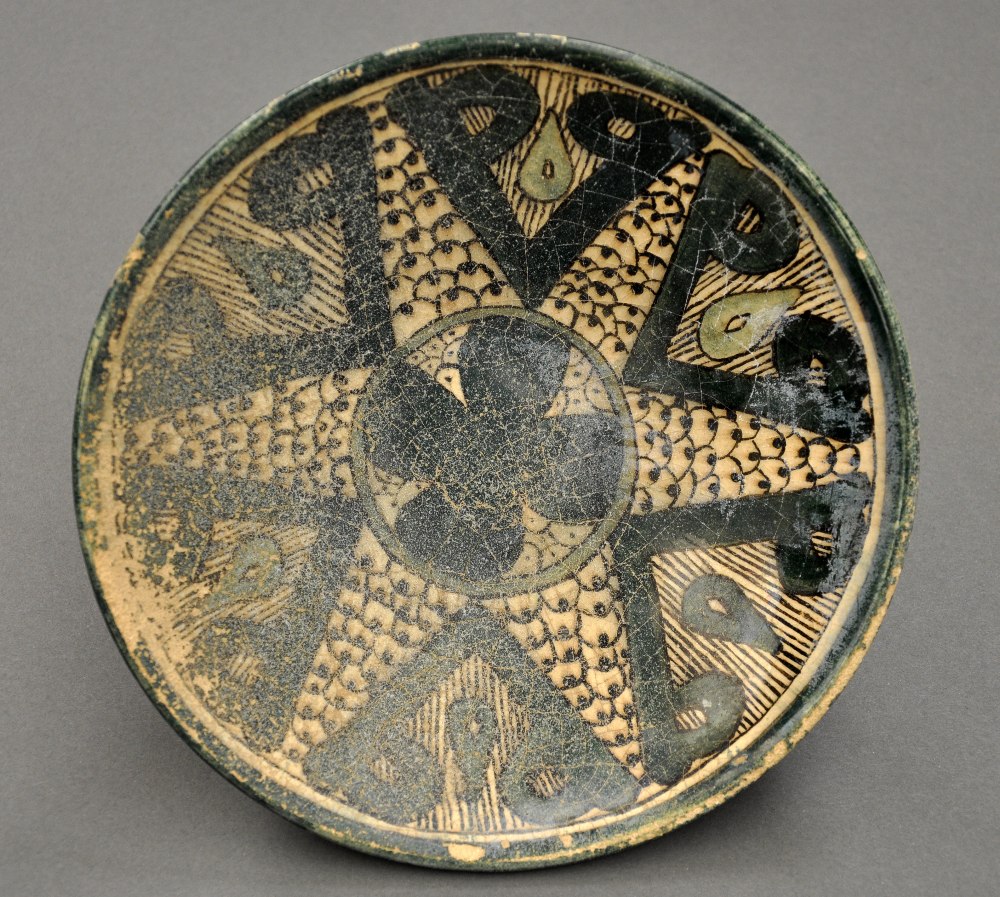 A C12/C13th Raqqa green cream and black glazed bowl with central stylised flowerhead motif